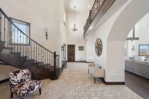 Foyer featuring an inviting chandelier, a towering ceiling, visible vents, and stairway