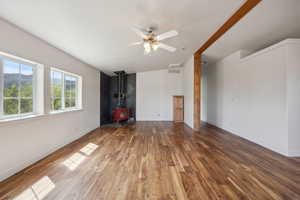 Unfurnished living room featuring a wood stove, visible vents, baseboards, wood finished floors, and a ceiling fan