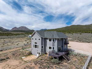 Rear view of house featuring a rural view, a deck with mountain view, fence, roof with shingles, and central AC