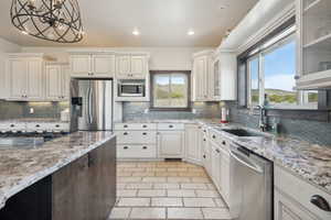 Kitchen with a sink, light stone counters, stainless steel appliances, and decorative backsplash