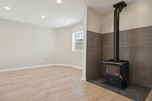 Unfurnished living room with a wood stove, recessed lighting, wood finished floors, and baseboards