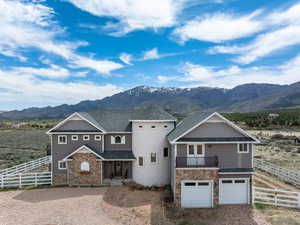 View of front of home with a mountain view, driveway, stone siding, and fence