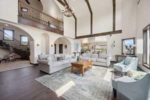 Living room with wood finished floors, arched walkways, stairs, baseboards, and high vaulted ceiling