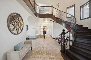 Foyer entrance with stairway, brick patterned floor, visible vents, a towering ceiling, and arched walkways