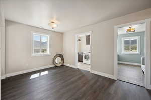 Unfurnished bedroom with baseboards, washer / clothes dryer, multiple windows, and dark wood-type flooring