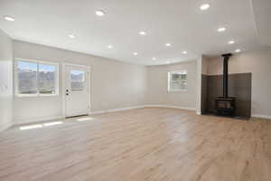 Unfurnished living room with recessed lighting, light wood finished floors, a wood stove, and baseboards