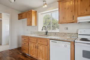 Kitchen featuring light stone countertops, a sink, under cabinet range hood, and white appliances