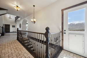 Hallway featuring arched walkways, an upstairs landing, brick floor, and a chandelier