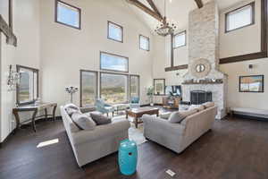 Living area featuring beamed ceiling, an inviting chandelier, a fireplace, high vaulted ceiling, and dark wood finished floors