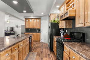 Kitchen with a sink, dark wood finished floors, dark countertops, decorative backsplash, and black appliances