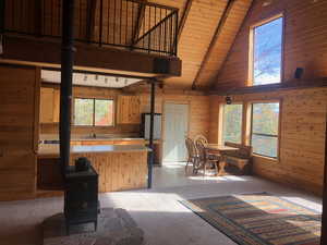 Kitchen featuring beamed ceiling, a wood stove, light colored carpet, light countertops, and wooden walls
