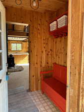 Mudroom with tile patterned floors, wooden ceiling, a wood stove, and wooden walls
