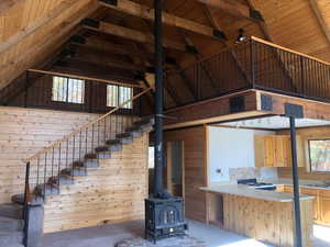 Unfurnished living room featuring a wood stove, carpet flooring, wooden ceiling, high vaulted ceiling, and wood walls