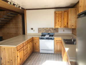 Kitchen featuring a sink, white range with gas stovetop, a peninsula, freestanding refrigerator, and light floors