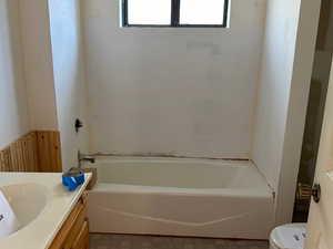 Full bathroom featuring a wainscoted wall, toilet, a bathing tub, and vanity