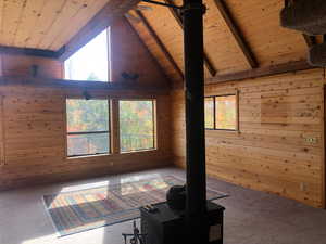 Unfurnished living room featuring wood walls, lofted ceiling with beams, carpet, and wood ceiling