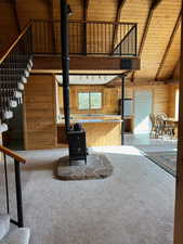 Living area with a wood stove, carpet flooring, beam ceiling, wooden walls, and wood ceiling