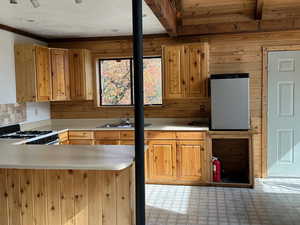 Kitchen with a sink, a peninsula, light countertops, gas stove, and freestanding refrigerator