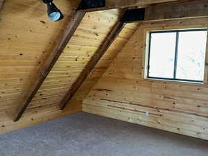 Bonus room featuring wooden walls, lofted ceiling with beams, carpet flooring, and wooden ceiling