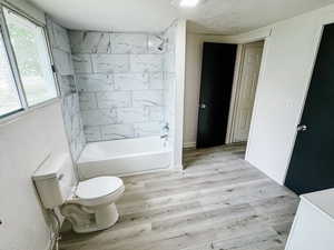 Full bathroom featuring shower / tub combination, a textured ceiling, wood finished floors, and toilet