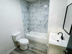 Full bath with toilet, wood finished floors, vanity, and a textured wall