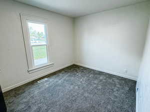 Empty room featuring dark colored carpet, visible vents, and baseboards