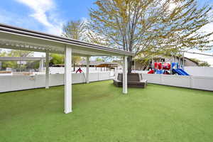 View of yard with fence, a hot tub, and a playground