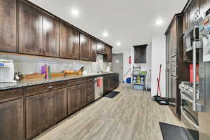 Kitchen featuring light wood-style flooring, appliances with stainless steel finishes, dark brown cabinets, light stone countertops, and recessed lighting