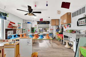 Kitchen with a textured ceiling, ceiling fan, freestanding refrigerator, light wood-type flooring, and brown cabinetry