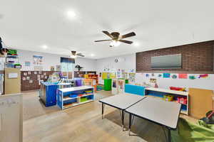 Rec room with wood finished floors, ceiling fan, brick wall, and a textured ceiling