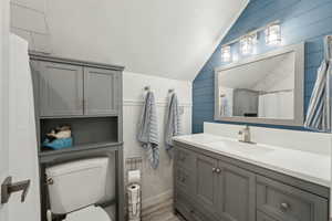 Full bath featuring wooden walls, toilet, wood finished floors, vaulted ceiling, and vanity
