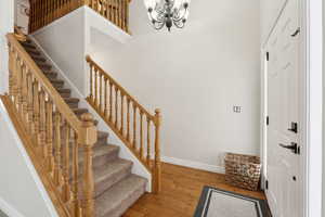 Entryway featuring baseboards, wood finished floors, a high ceiling, stairs, and a notable chandelier