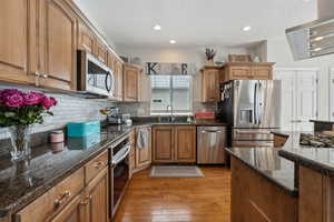 Kitchen featuring decorative backsplash, appliances with stainless steel finishes, a sink, dark stone countertops, and light wood-type flooring