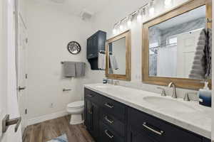 Full bath with toilet, double vanity, a sink, and wood finished floors