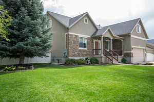 View of front of property featuring stucco siding, roof with shingles, a front lawn, and stone siding