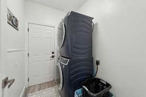 Clothes washing area featuring light wood-type flooring, stacked washer / dryer, and laundry area