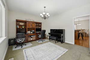 Carpeted home office with baseboards, visible vents, and an inviting chandelier