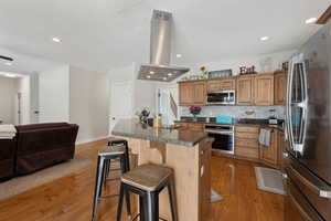 Kitchen with island range hood, dark countertops, a kitchen island, a breakfast bar area, and stainless steel appliances
