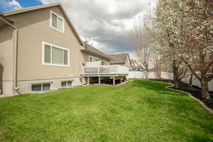 Rear view of property with stucco siding, a deck, a yard, and a fenced backyard