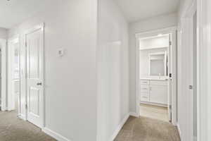 Corridor with baseboards, a sink, visible vents, and light carpet