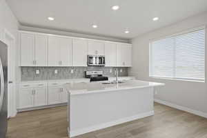 Kitchen featuring light countertops, stainless steel appliances, decorative backsplash, and a sink