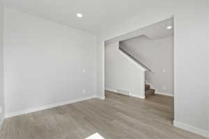 Unfurnished living room featuring light wood-style floors, baseboards, stairs, and visible vents