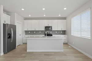 Kitchen featuring a sink, light countertops, an island with sink, stainless steel appliances, and decorative backsplash