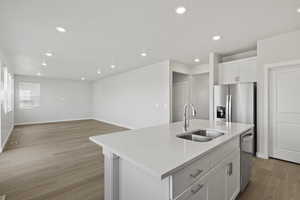 Kitchen featuring a sink, light wood-style floors, stainless steel appliances, white cabinetry, and a center island with sink