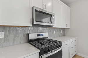 Kitchen with light stone counters, white cabinetry, appliances with stainless steel finishes, and tasteful backsplash