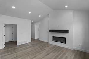 Unfurnished living room with recessed lighting, light wood-style floors, a glass covered fireplace, visible vents, and vaulted ceiling