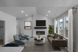 Living room featuring recessed lighting, lofted ceiling, wood finished floors, and a glass covered fireplace