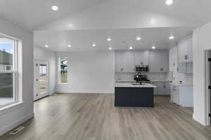Kitchen featuring stainless steel microwave, light countertops, vaulted ceiling, visible vents, and a center island with sink