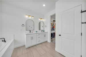 Bathroom with a sink, a walk in closet, double vanity, a washtub, and baseboards