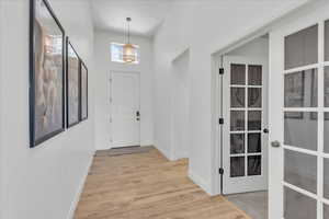 Entryway with an inviting chandelier, baseboards, french doors, and light wood-style flooring
